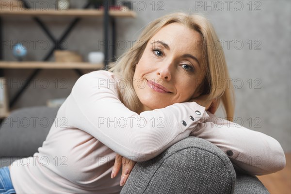 Smiling portrait young woman leaning gray sofa