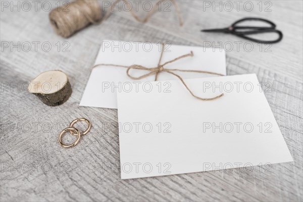 Spool miniature tree stump wedding rings scissor white envelope wooden background
