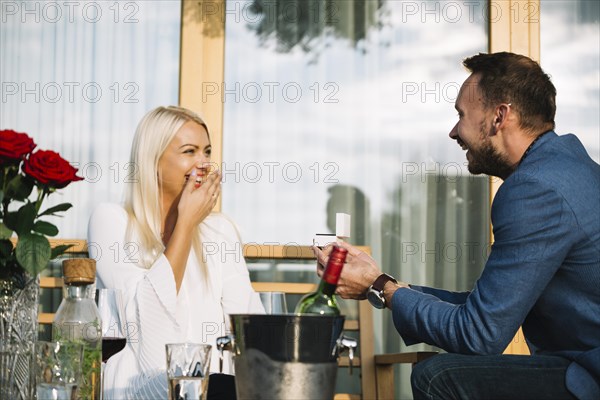 Surprised young woman looking man giving engagement ring restaurant