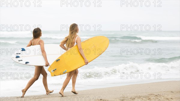 Two smiley friends running beach with surfboards