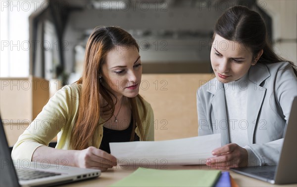 Two young businesswoman looking paper office