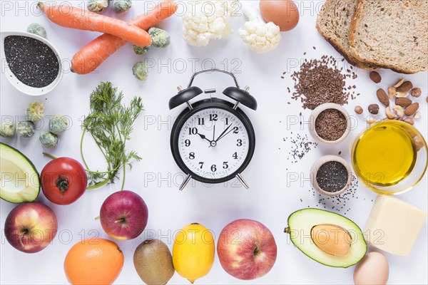 Variety ingredients with alarm clock arranged against isolated white background
