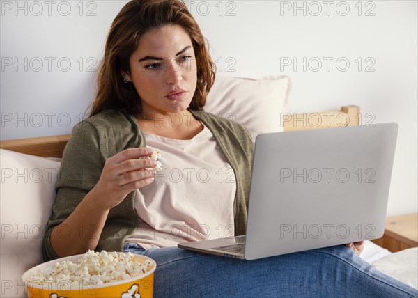 Woman eating popcorn while watching movie laptop