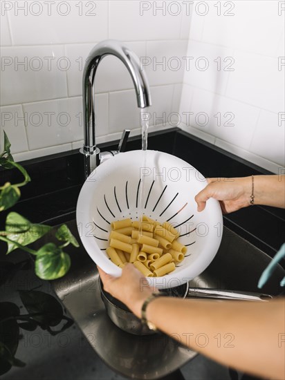 Woman washing rigatoni pasta white colander faucet sink