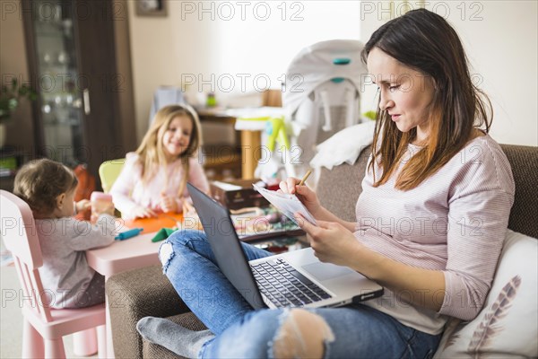 Woman writing notes while using laptop
