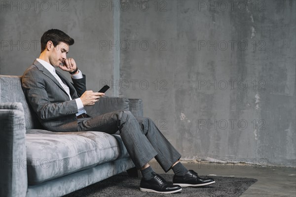 Young businessman sitting grey sofa using cellphone