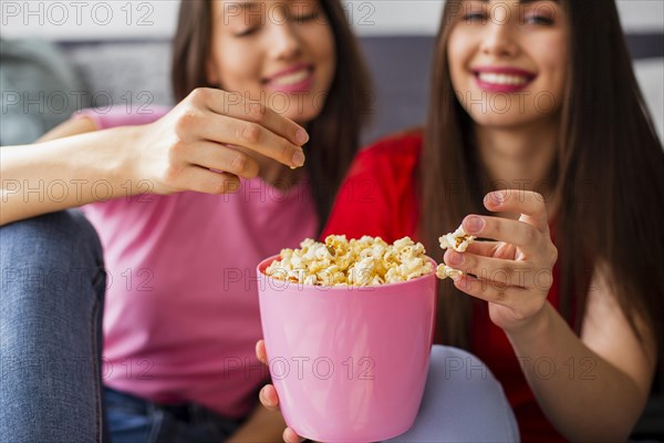 Young girlfriends home eating popcorn