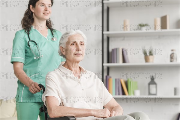 Young nurse assisting disabled senior woman sitting wheel chair