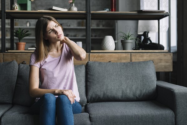 Young woman sitting sofa having neck pain