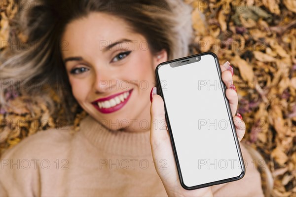 Attractive woman lying dry leaves showing blank screen cellphone