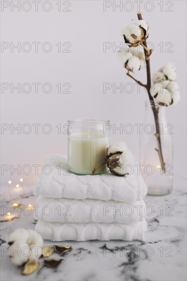 Candle candleholder with stacked napkins near cotton twig lighting equipments marble surface