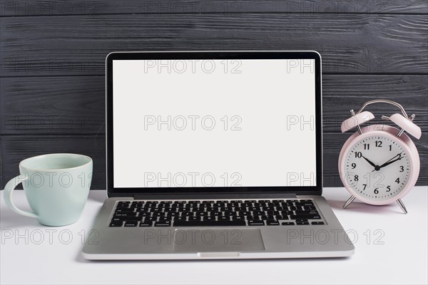 Ceramics cup alarm clock open laptop white desk against wooden black background