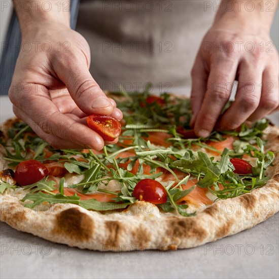 Close up man putting tomatoes baked pizza dough with smoked salmon slices