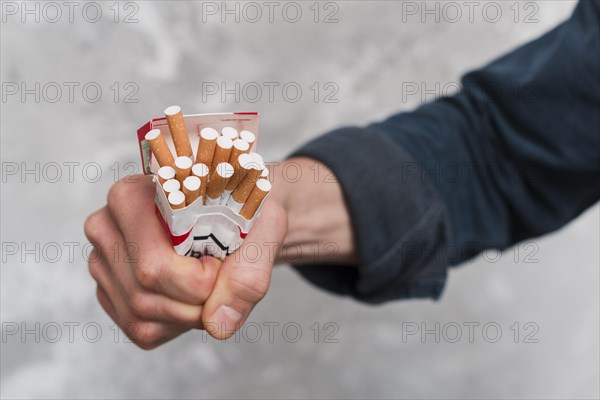 Close up man s hand crushing cigarettes box