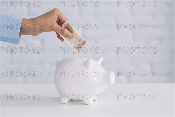 Close up person s hand inserting fifty euro banknote piggybank desk