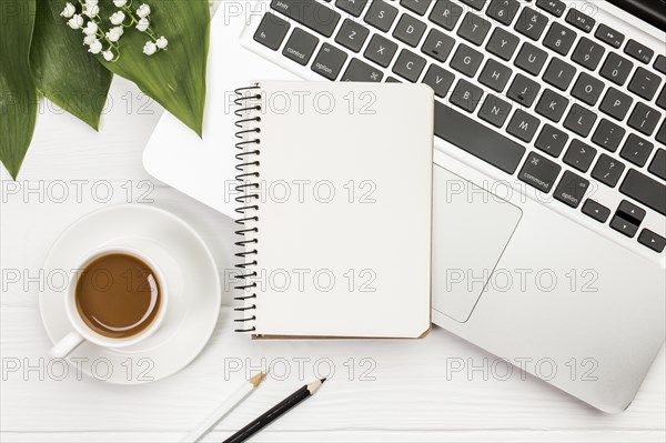 Coffee cup with spiral notepad laptop with colored pencils office wooden desk