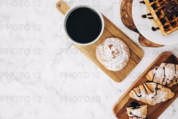Elevated view coffee cup baked buns croissant waffles wooden tray against marble textured background
