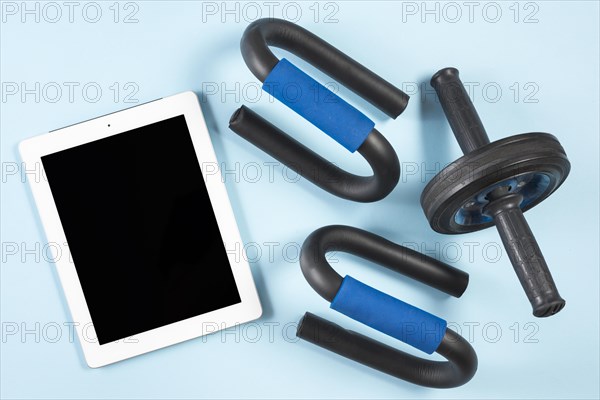 Elevated view digital tablet with fitness roller push up bar blue background