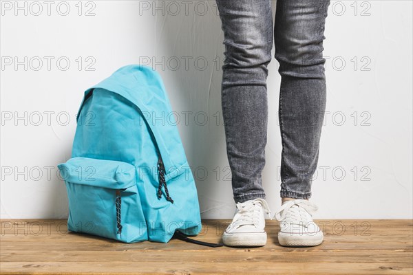 Faceless person standing beside schoolbag wooden table