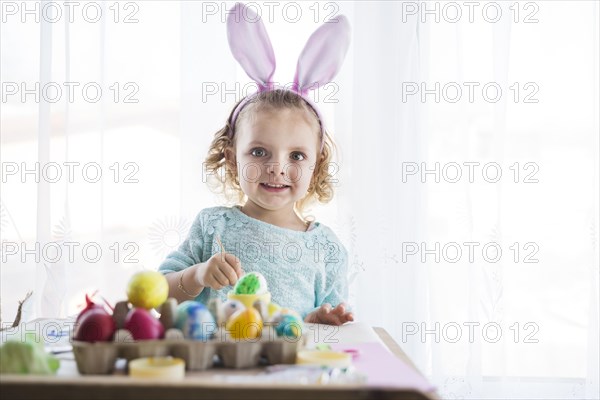 Girl with rabbit ears coloring eggs