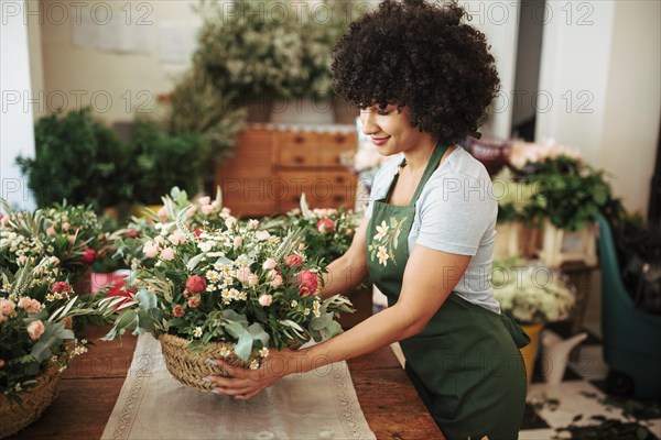 Happy african woman arranging basket flowers desk