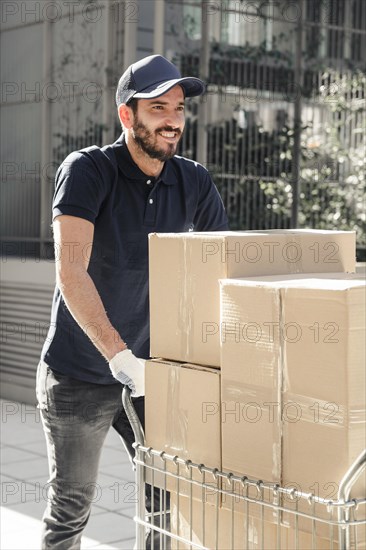 Happy delivery man with cardboard boxes walking sidewalk