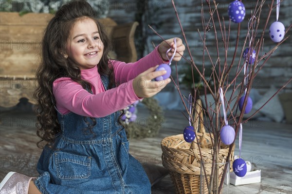 Happy girl hanging easter eggs branch