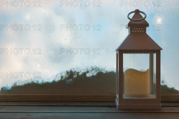 Lantern with candle wood board near bank snow through window