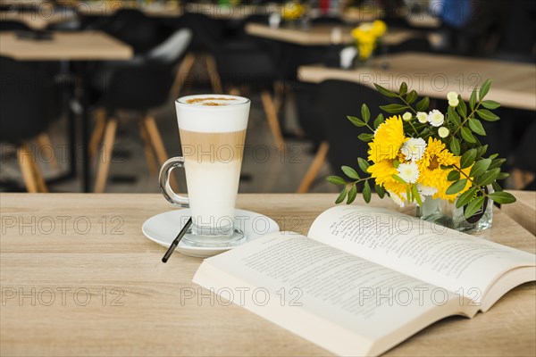 Open book with latte coffee cup fresh flower vase wooden table