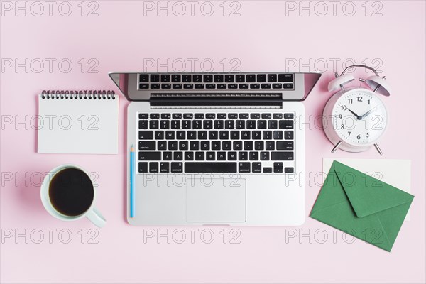 Open laptop pencil alarm clock spiral notepad envelope pink background