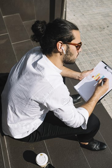 Overhead view businessman sitting staircase drawing graph clipboard