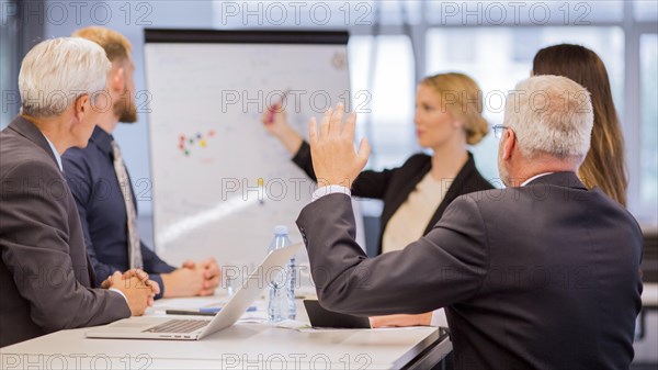 Rear view senior businessman asking questions during presentation