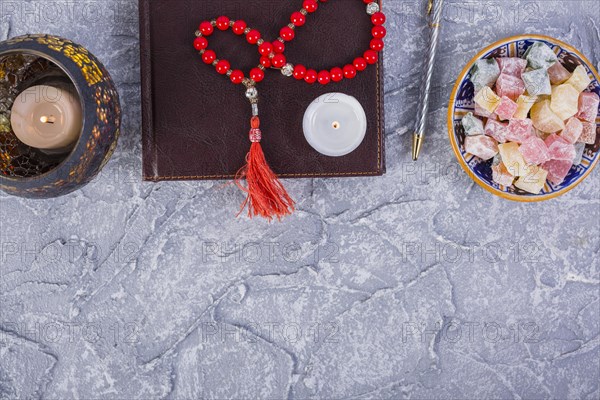 Red prayer beads candle diary pen lighted candle with bowl rakhat lukum rough grey textured background