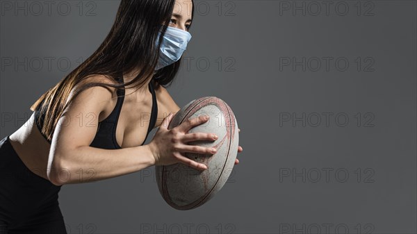 Side view athletic female rugby player holding ball while wearing medical mask