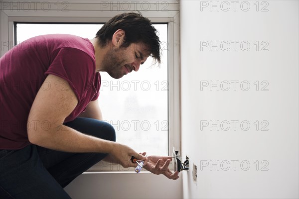 Side view electrician fixing plug socket white wall