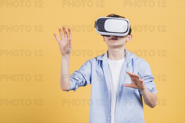 Smile boy wearing using virtual reality glasses headset moving his hands air against yellow background