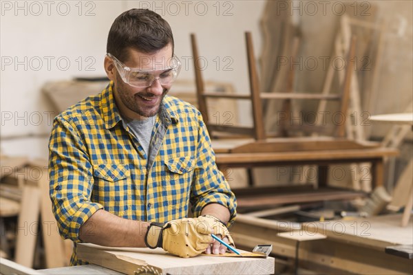 Smiling professional male carpenter measuring wooden block with ruler