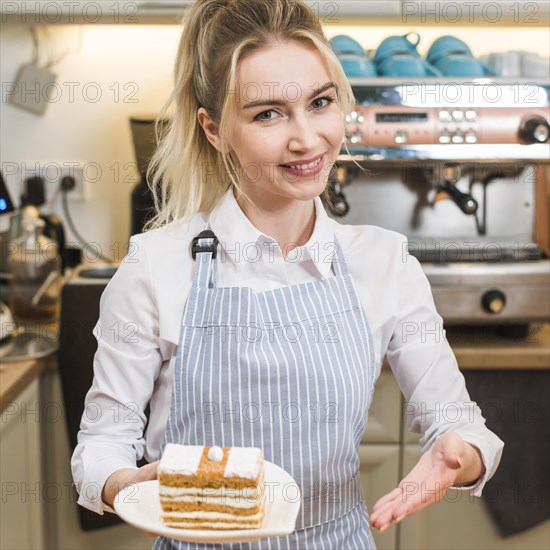 Smiling young woman presenting cake slice coffee shop
