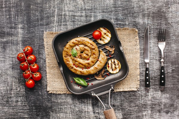 Spiral yummy grilled sausages pan with vegetable textured background