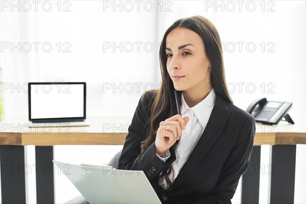 Thoughtful young businesswoman with pen clipboard her hand