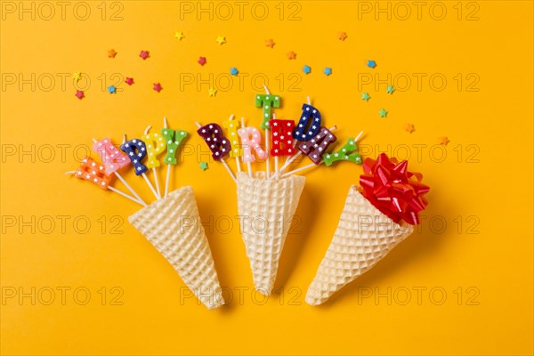 Three waffle cones ribbon bow happy birthday text candles with sprinkles yellow backdrop