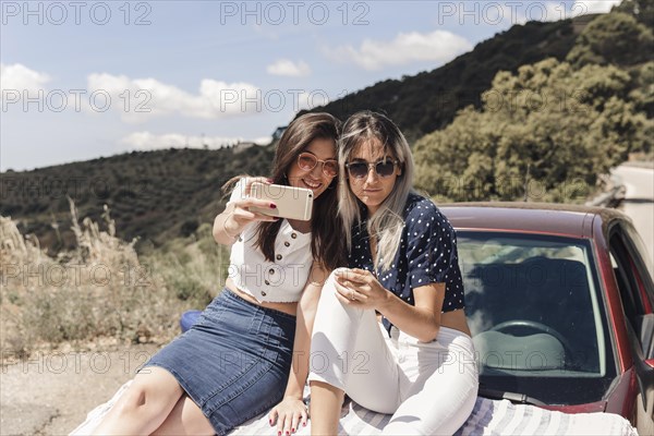 Trendy female friends sitting car taking selfie