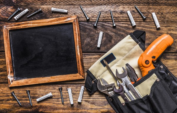 Various tools toolbag near blank slate bolts wooden background