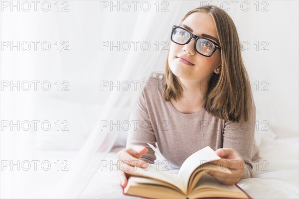 Woman lying bed with book daydreaming