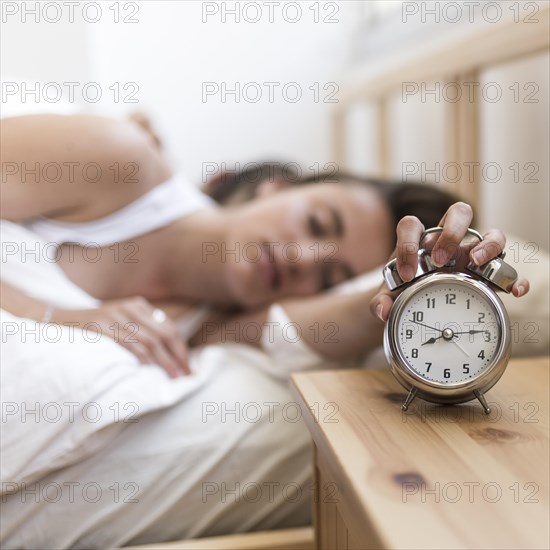 Woman sleeping bed turning off alarm clock