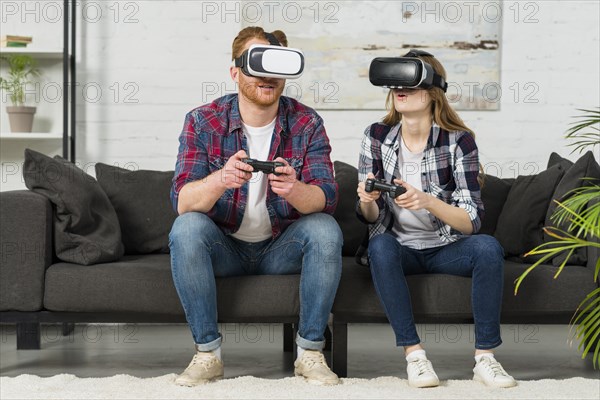 Young couple wearing virtual reality goggles playing video game living room