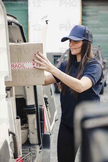 Young female courier unloaded cardboard box from vehicle