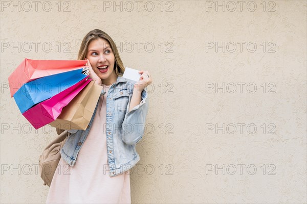 Amazed woman standing with shopping bags credit card wall