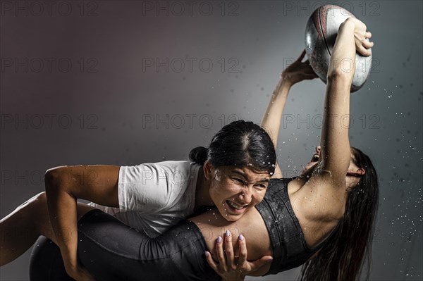 Athletic wet female rugby players fighting ball