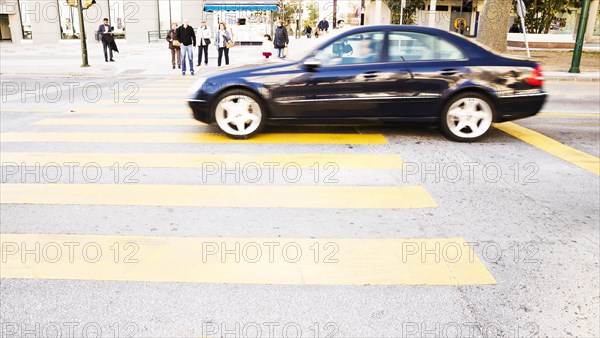 Black car driving road with yellow zebra crossing
